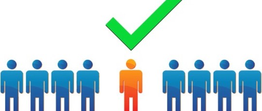 grafika przedstawia dziewięć osób w kolorze niebieskim stojących równo w jednym rzędzie z których jedna osoba stojąca na środku jest wyróżniona kolorem pomarańczowym i zamieszczony jest nad jej głową symbol zaznaczenia wyboru tzw. fajka